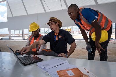 Three men looking into a notebook at a construction site 